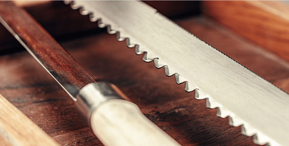 The image illustrates a serrated knife, showcasing its unique serrated edge with small teeth designed for cutting through tough crusts and soft foods without crushing them. The knife features one flat side and one beveled side, emphasizing the need for careful sharpening techniques specific to serrated knives, using tools like a tapered diamond rod to maintain the correct angle and avoid damaging the blade's profile.