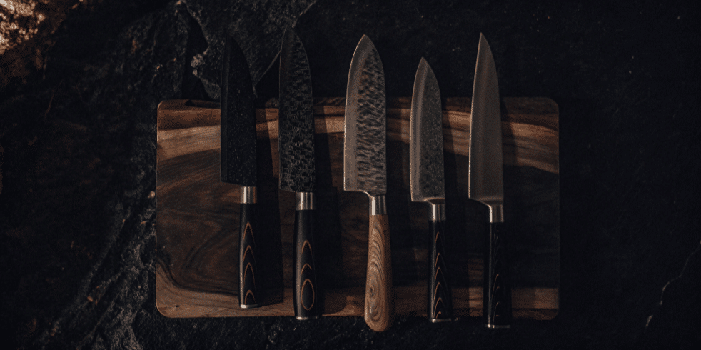 The image showcases a variety of Japanese vegetable knives, including a nakiri knife and a santoku knife, displayed on a wooden cutting board. Each knife features a sharp blade, highlighting their sleek designs and precision for cutting vegetables, demonstrating their importance in kitchen prep for home cooks and professional chefs alike.