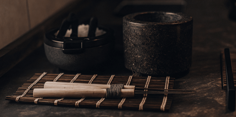 The image showcases essential Japanese kitchen tools including a rice cooker, bamboo sushi mat, sushi oke, and a Japanese-style mortar, all arranged on a sturdy cutting board. These versatile gadgets are designed to enhance the cooking process, making it easier to prepare authentic Japanese dishes like sushi rolls and miso soup.