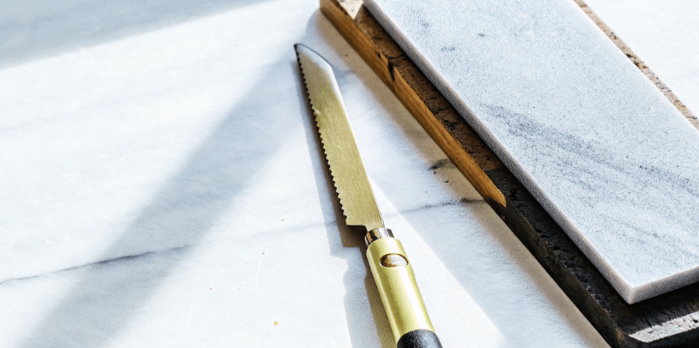 The image shows a clean serrated knife placed on a stable surface, ready for sharpening. A permanent marker is used to color the serrations on the beveled edge, ensuring the user can see where the sharpening rod makes contact and maintain the correct angle while honing the blade.