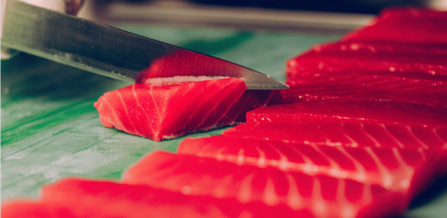 Using Sujihiki Knife - Japanes Knives Tips A sujihiki knife, known for its razor sharp edge and narrow blade, is expertly slicing through raw fish for sushi, showcasing its ability to produce paper thin slices with precision. The pointed tip allows for delicate cuts, while the smooth, steady motion ensures clean and precise results, making it an essential tool for sushi chefs and home cooks alike.