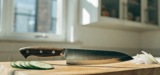 Premium Japanese Knive - Japanes Knives Tips An editorial style photo of a premium Japanese kitchen knife on a clean wooden cutting board in a bright home kitchen, natural window light, sliced vegetables nearby, sharp blade detail, minimal styling, high-end food blog look, horizontal composition